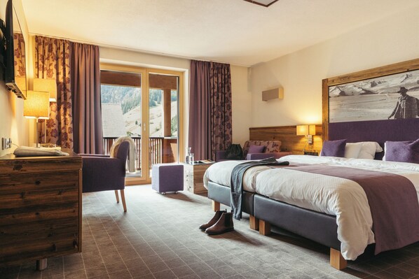 A hotel room with a large bed, a wooden dresser, a chair, a desk, and a window with curtains. - Hotel Kirchenwirt (Kaunertal)