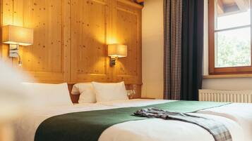 Habitación de hotel con cabecera de madera, dos lámparas de noche, un ventanal con cortinas y una cama bien tendida con sábanas blancas y una manta verde.