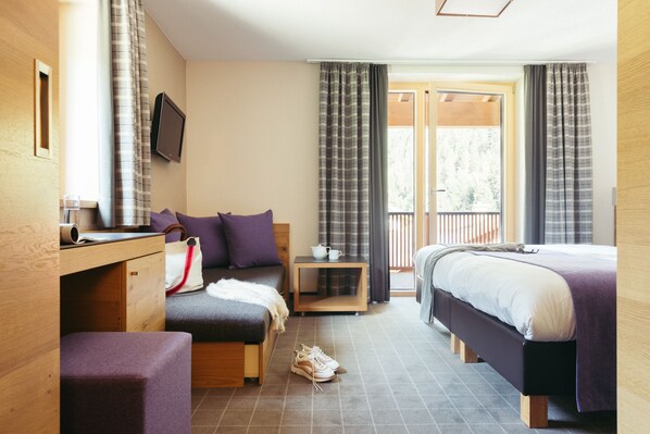 A hotel room with a bed, a desk, a chair, a small table, and a window with curtains. - Hotel Kirchenwirt (Kaunertal)