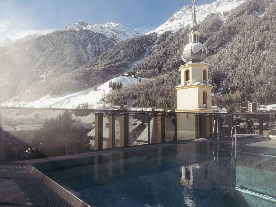 Una piscina con vistas a montañas nevadas y una torre de iglesia.