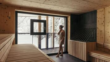 Ein Saunaraum mit Holzvertäfelung, einer Glastür zum Außenbereich und einer Saunabank.