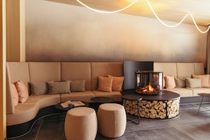 Un área de descanso moderna con un sofá curvo, otomanas y una chimenea central.