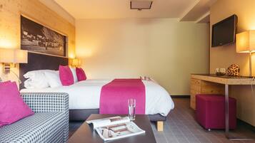 A hotel room with a bed, a desk, a chair, a coffee table, and a television.