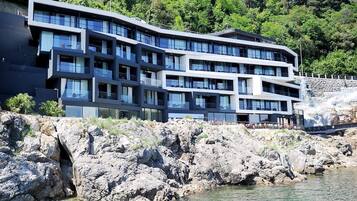 Um hotel moderno com vários andares e varandas, situado perto de um litoral rochoso e vegetação exuberante.