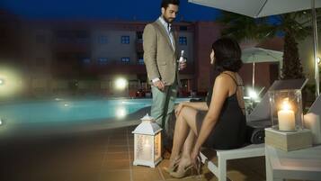 Un hombre y una mujer junto a una piscina, con un farol blanco y velas sobre una mesa.