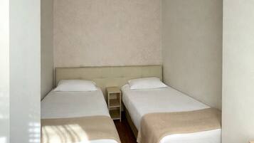 A small, well-lit room with two single beds, a nightstand, and a ceiling light.