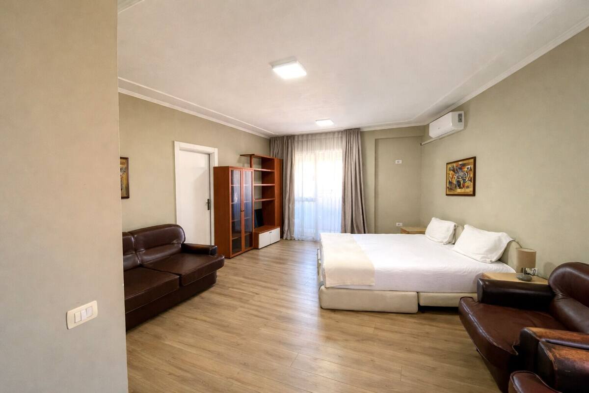 A hotel room with a bed, a sofa, a wardrobe, and a desk.