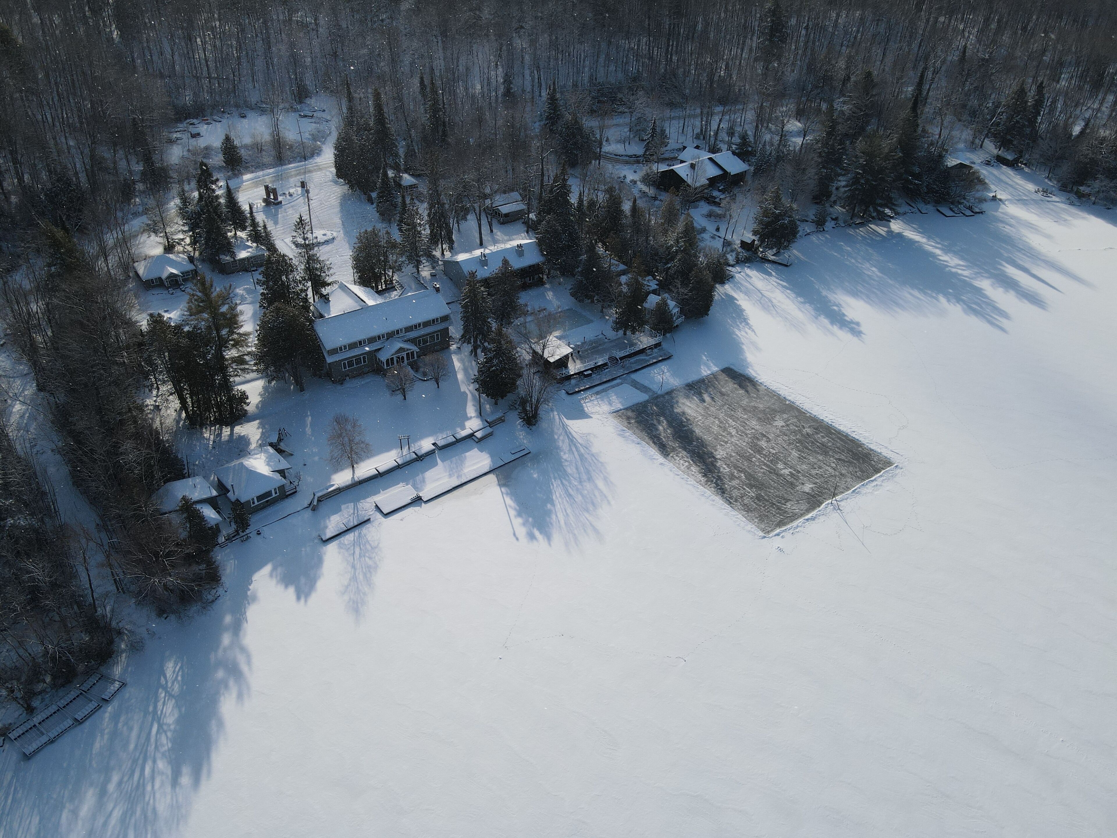 An aerial view of a snow-covered property with multiple buildings, a large open field, and a dense forest.