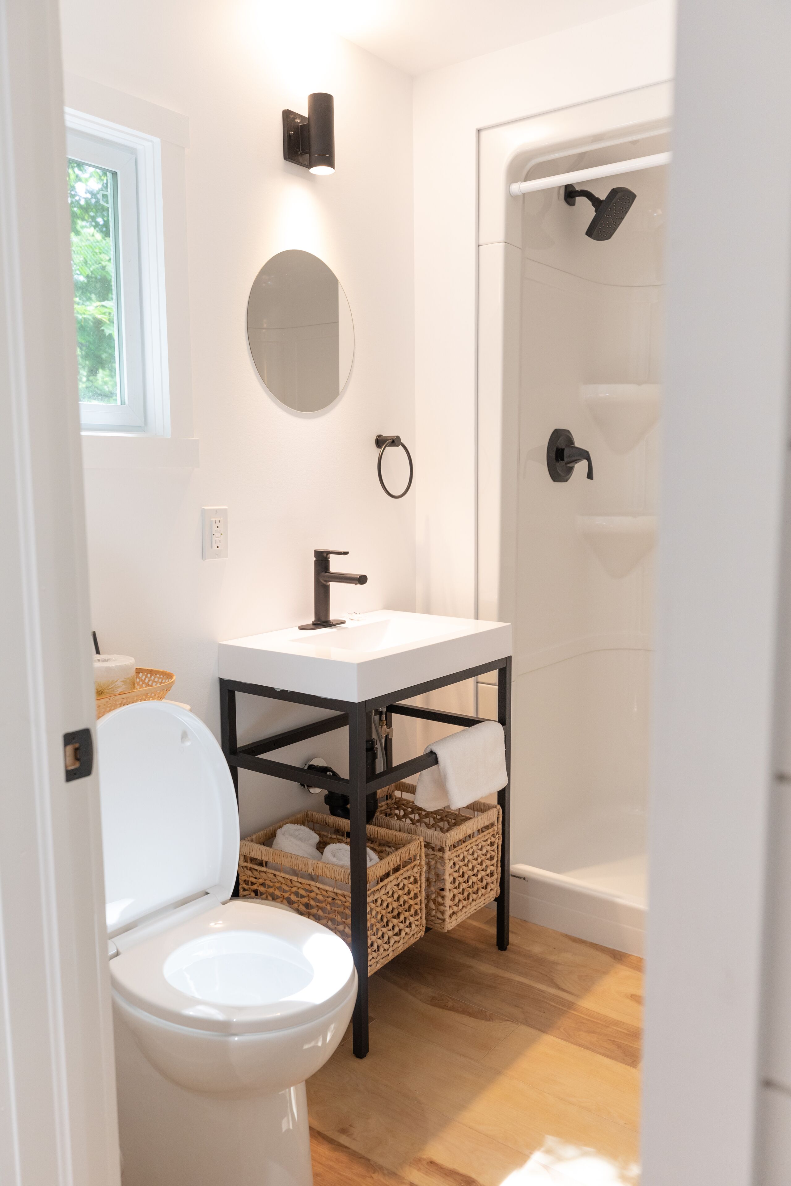 Un baño con inodoro, lavabo y ducha. Hay un ventanal sobre el inodoro, un espejo en la pared y un perchero para toallas.