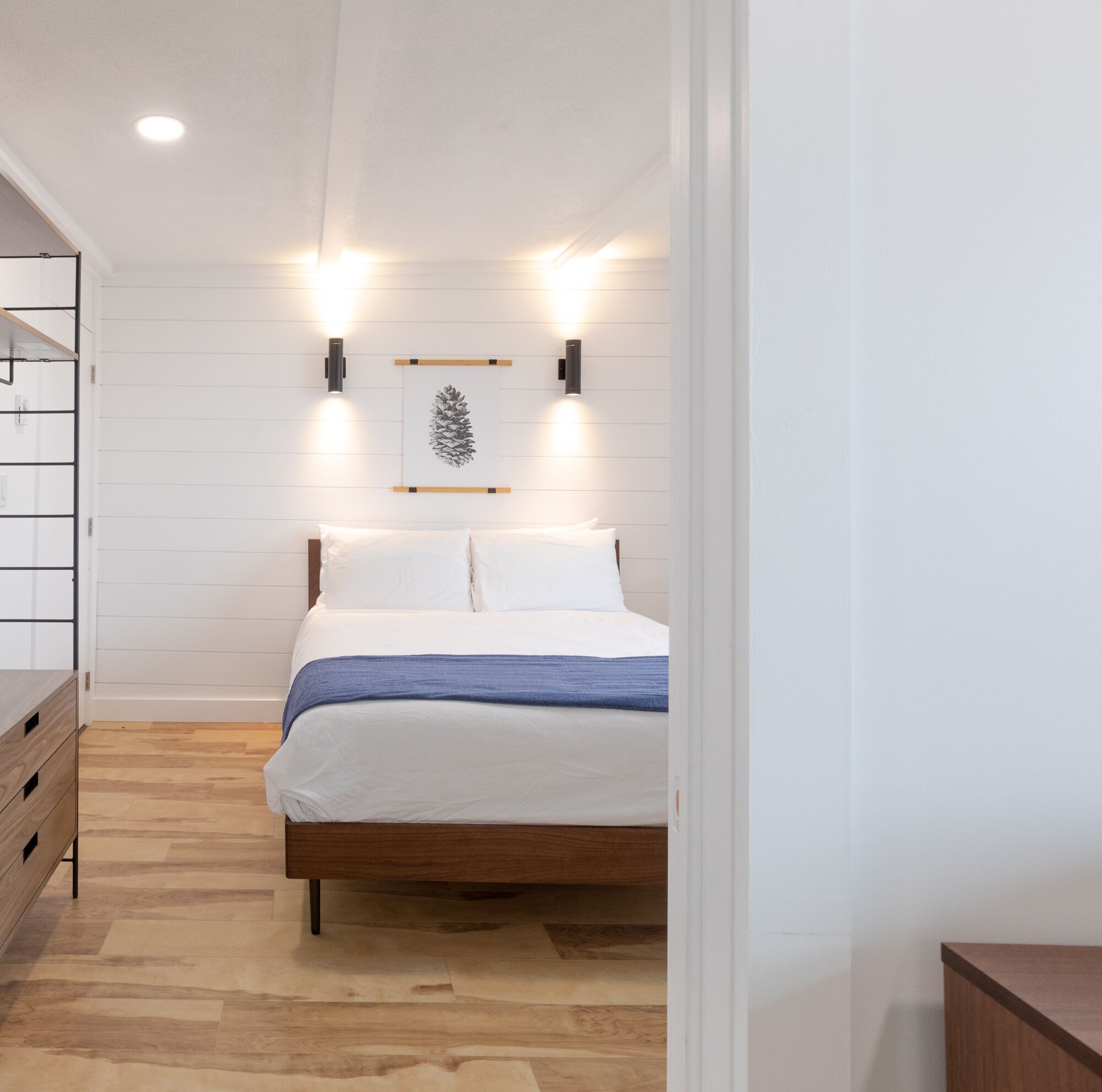 A bedroom with a wooden bed, white walls, and a pine cone artwork.