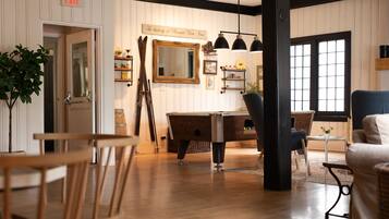 A room with a wooden floor, a billiards table, a mirror, and a chair.