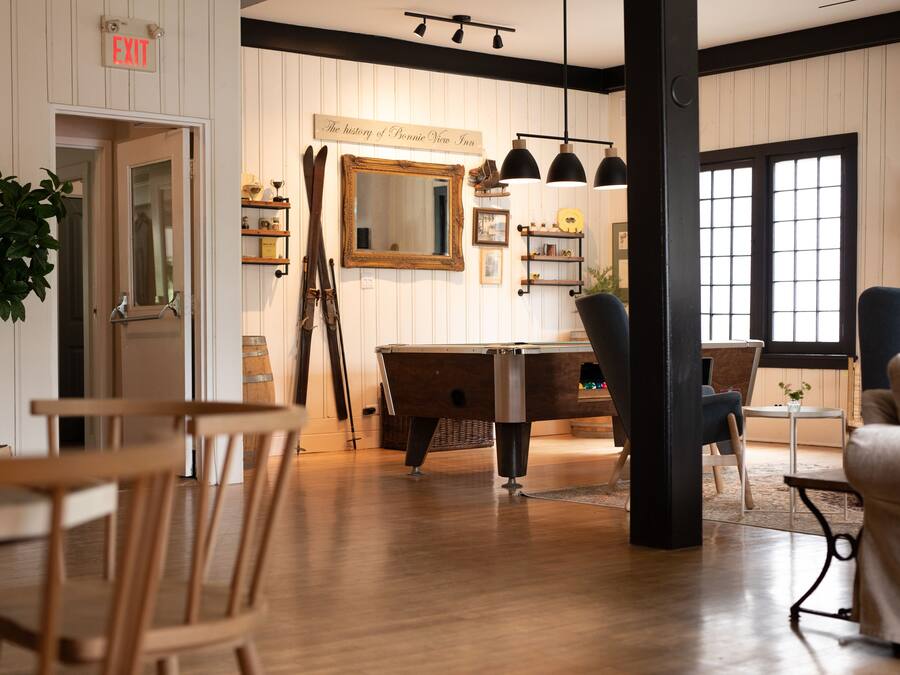 A room with a wooden floor, a billiards table, a mirror, and a chair.