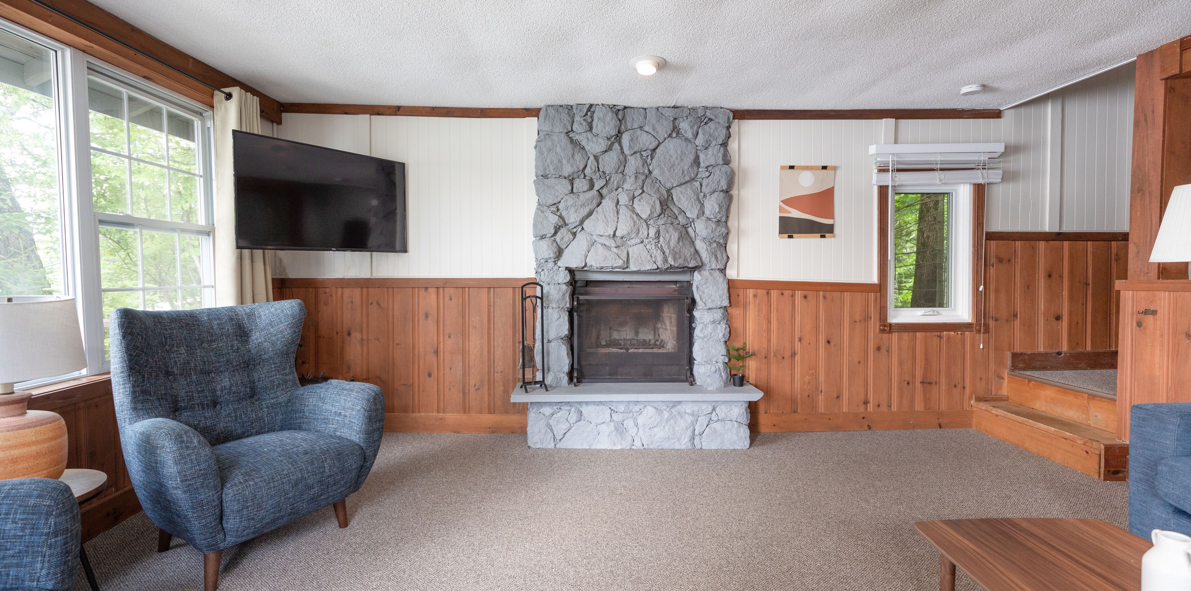 A cozy living room with a stone fireplace, wooden paneling, a television, and a comfortable chair.