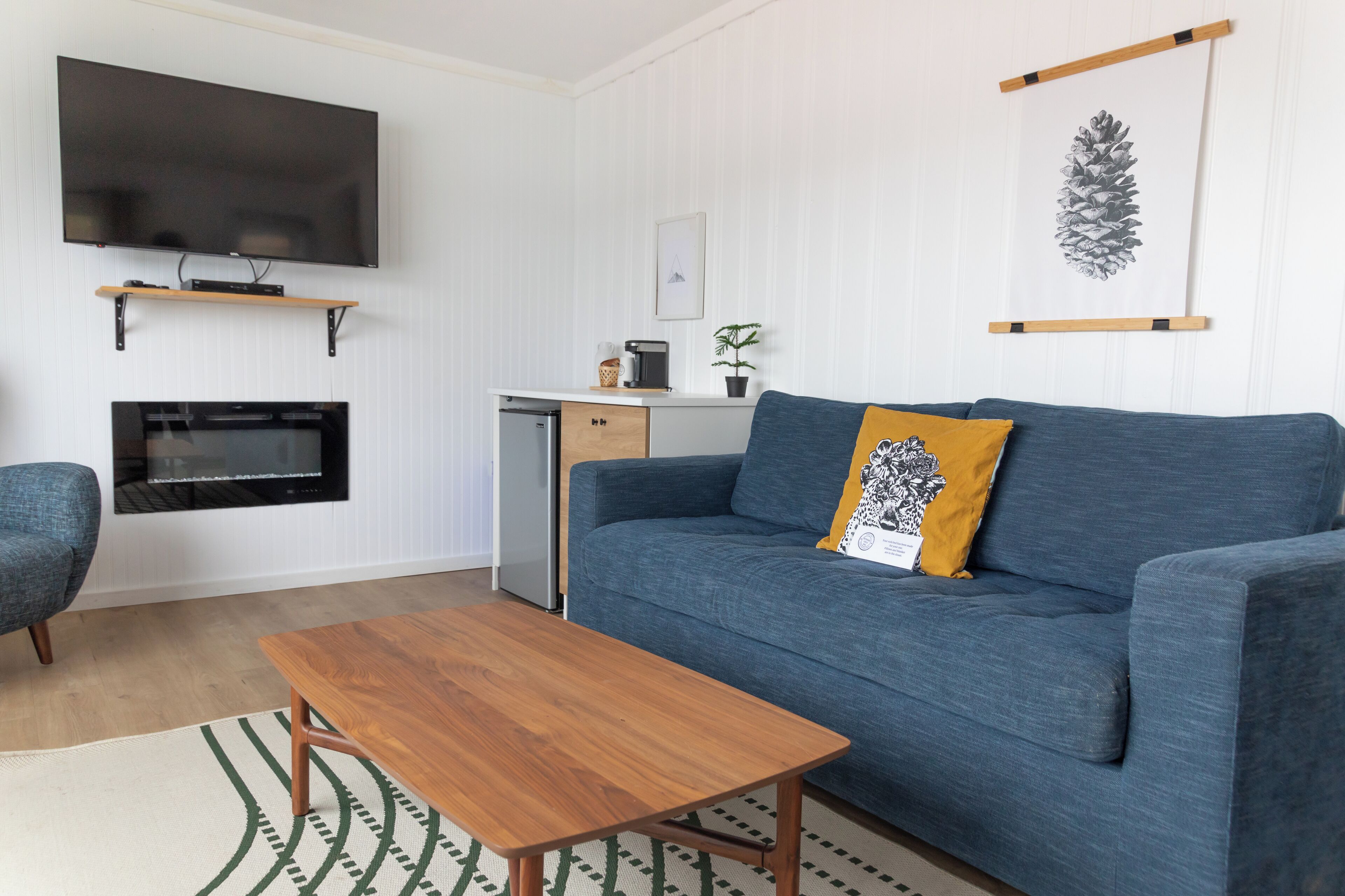 A modern living room with a blue sofa, wooden coffee table, and a flat-screen TV mounted above a fireplace.