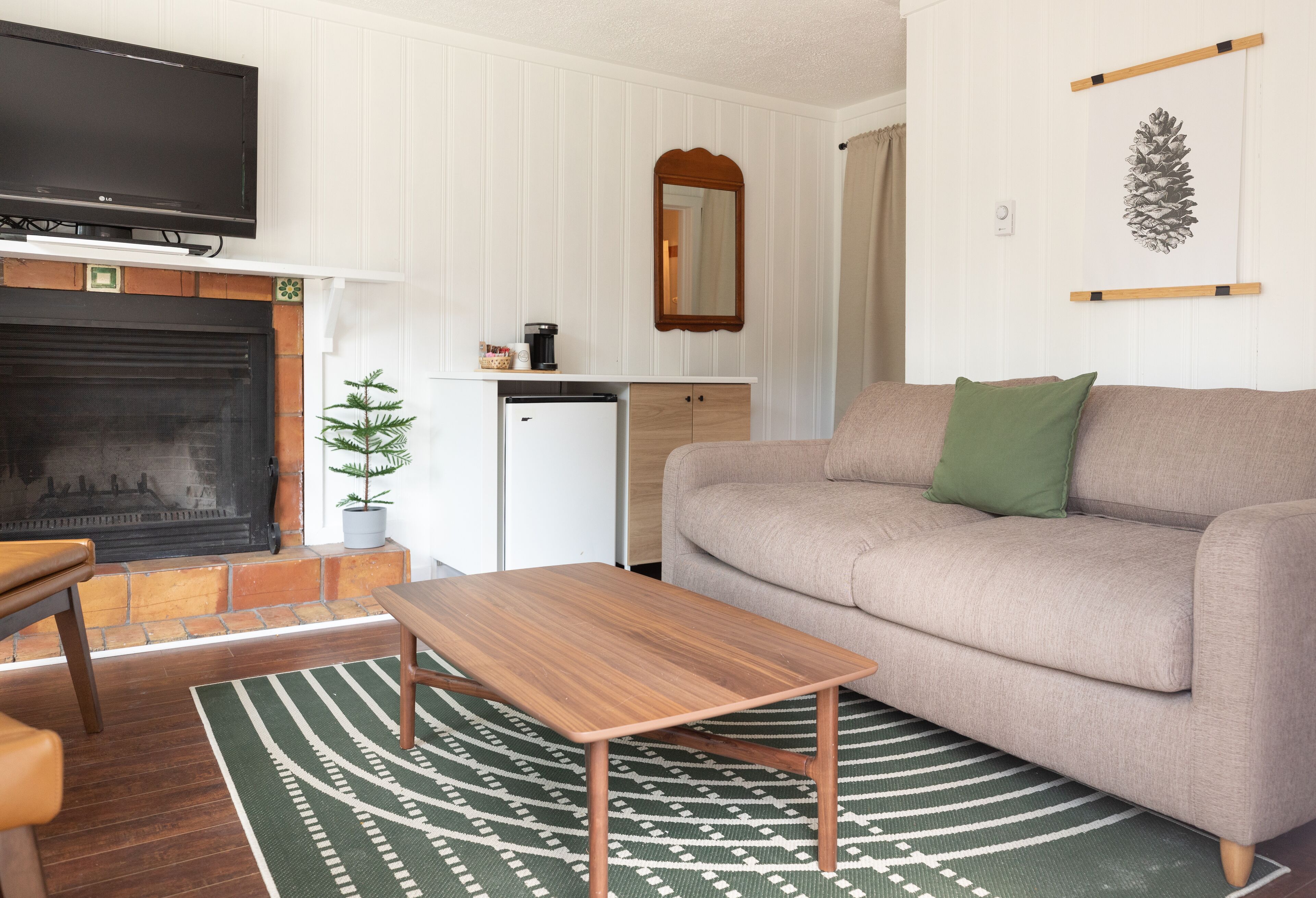 A living room with a fireplace, a television, a sofa, a coffee table, and a small refrigerator.