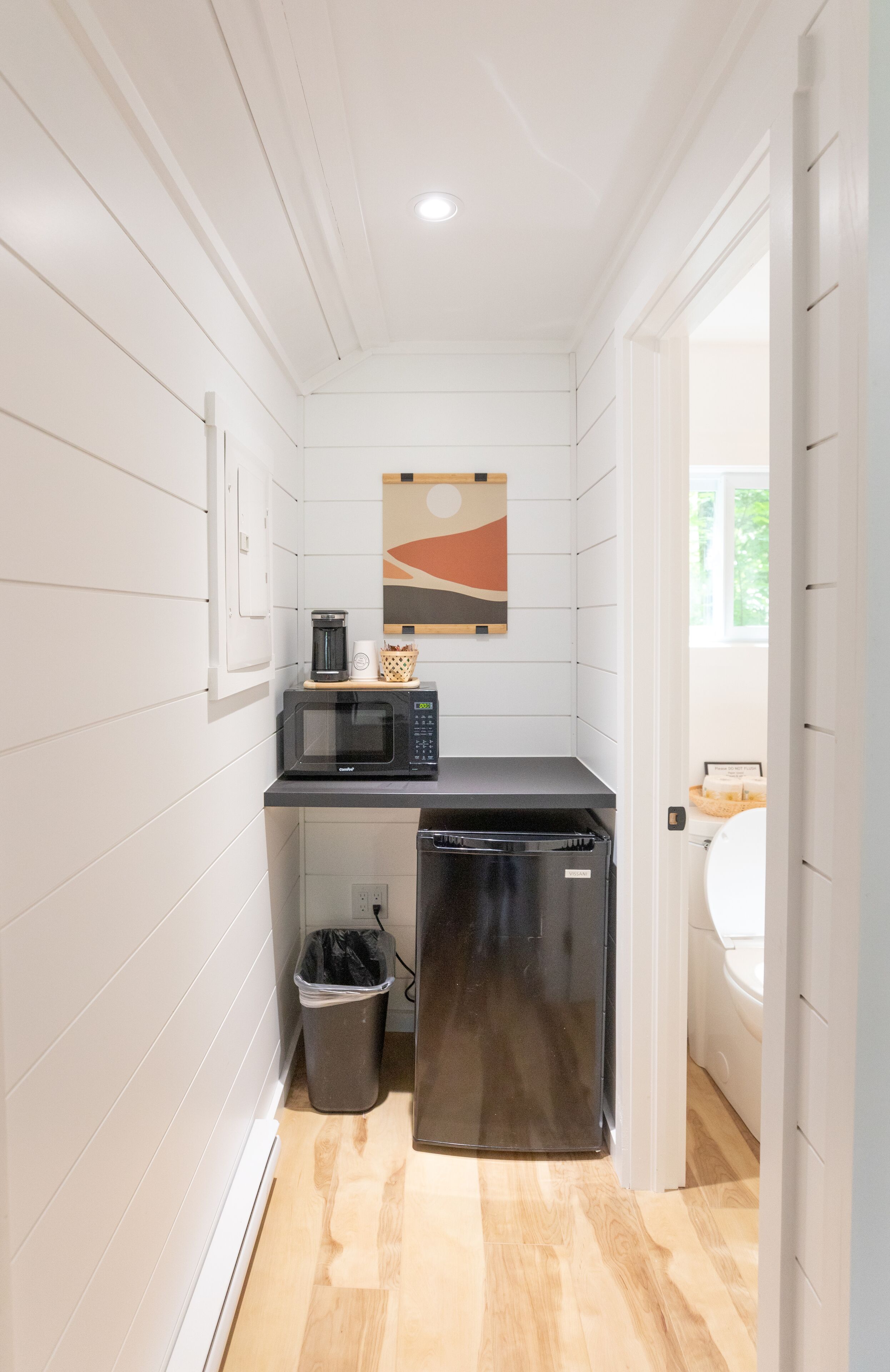 A compact kitchen with a microwave, coffee maker, and trash bin.