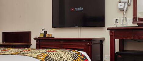 A hotel room with a bed, a TV mounted on the wall, a hairdryer on a table, and a wooden cabinet.