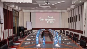 A conference room with a long table, chairs, water bottles, and a projector screen displaying "Best Western PLUS".
