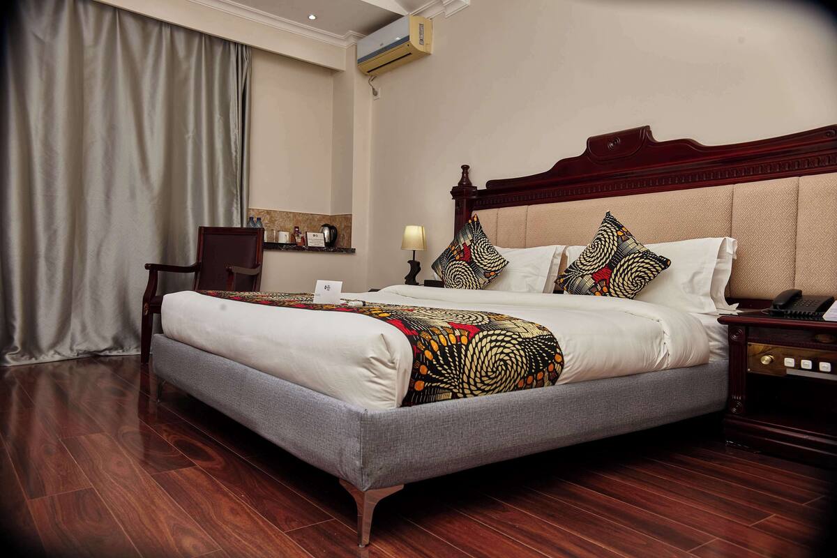 A hotel room with a large bed, a wooden nightstand, a desk, and a chair.