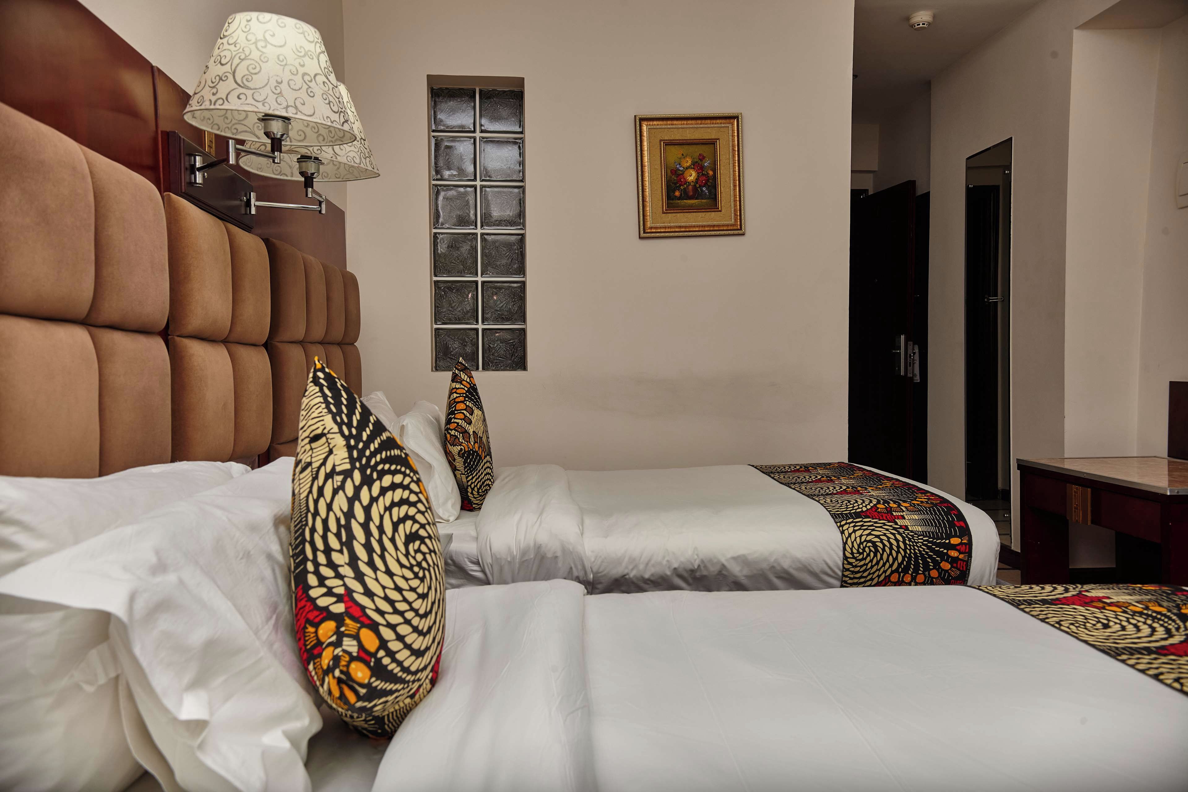 A hotel room with two beds, a window, a lamp, and a framed picture on the wall.