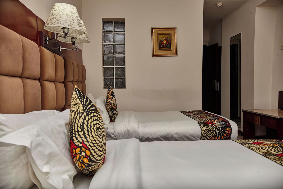 Habitación de hotel con dos camas, una ventana, una lámpara y un cuadro en la pared.