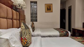 A hotel room with two beds, a window, a lamp, and a framed picture on the wall.