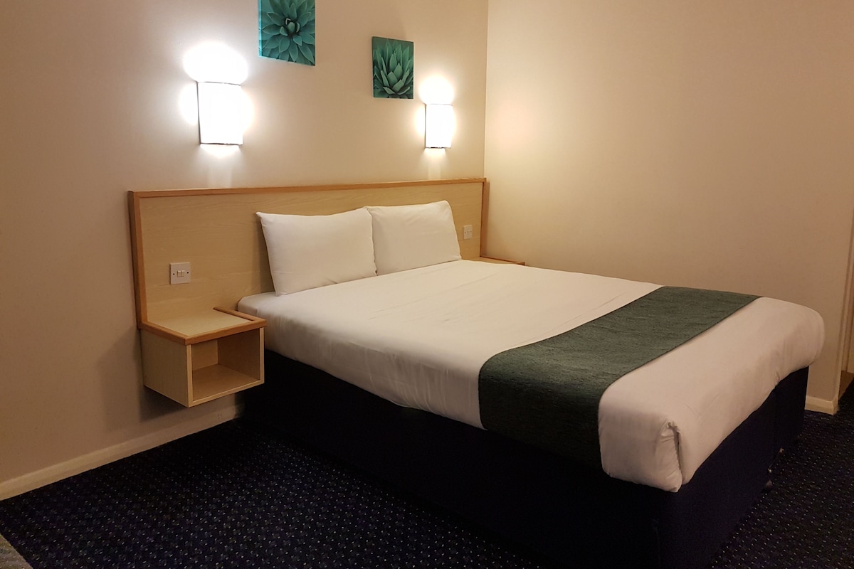 Et hotelværelse med seng, et natbord, to vægmonterede lamper og to billeder.