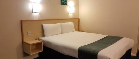 A hotel room with a bed, nightstand, two wall-mounted lights, and two wall art pieces.