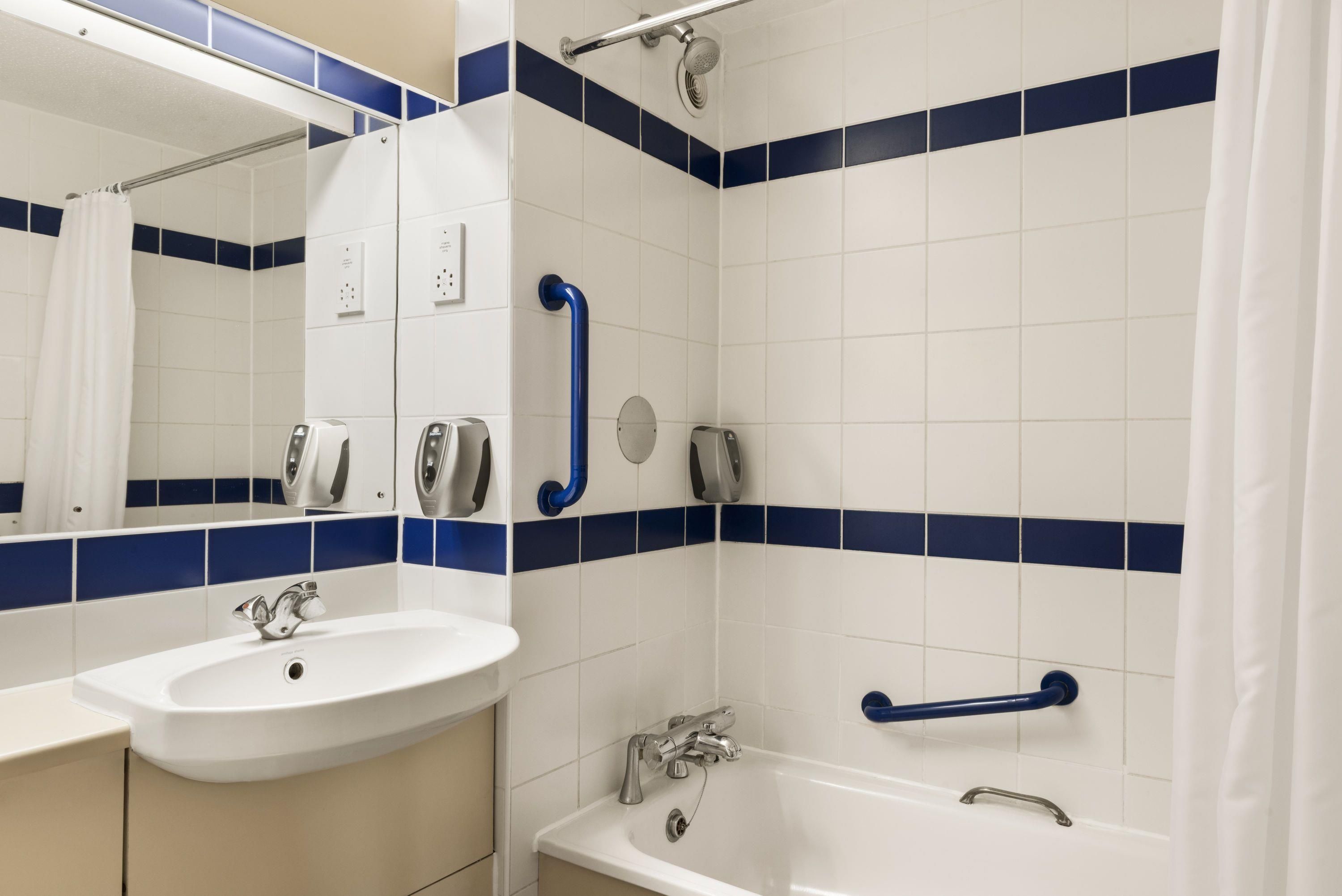 A bathroom with a white sink, a mirror, a shower with a handheld showerhead, and a bathtub with a grab bar.