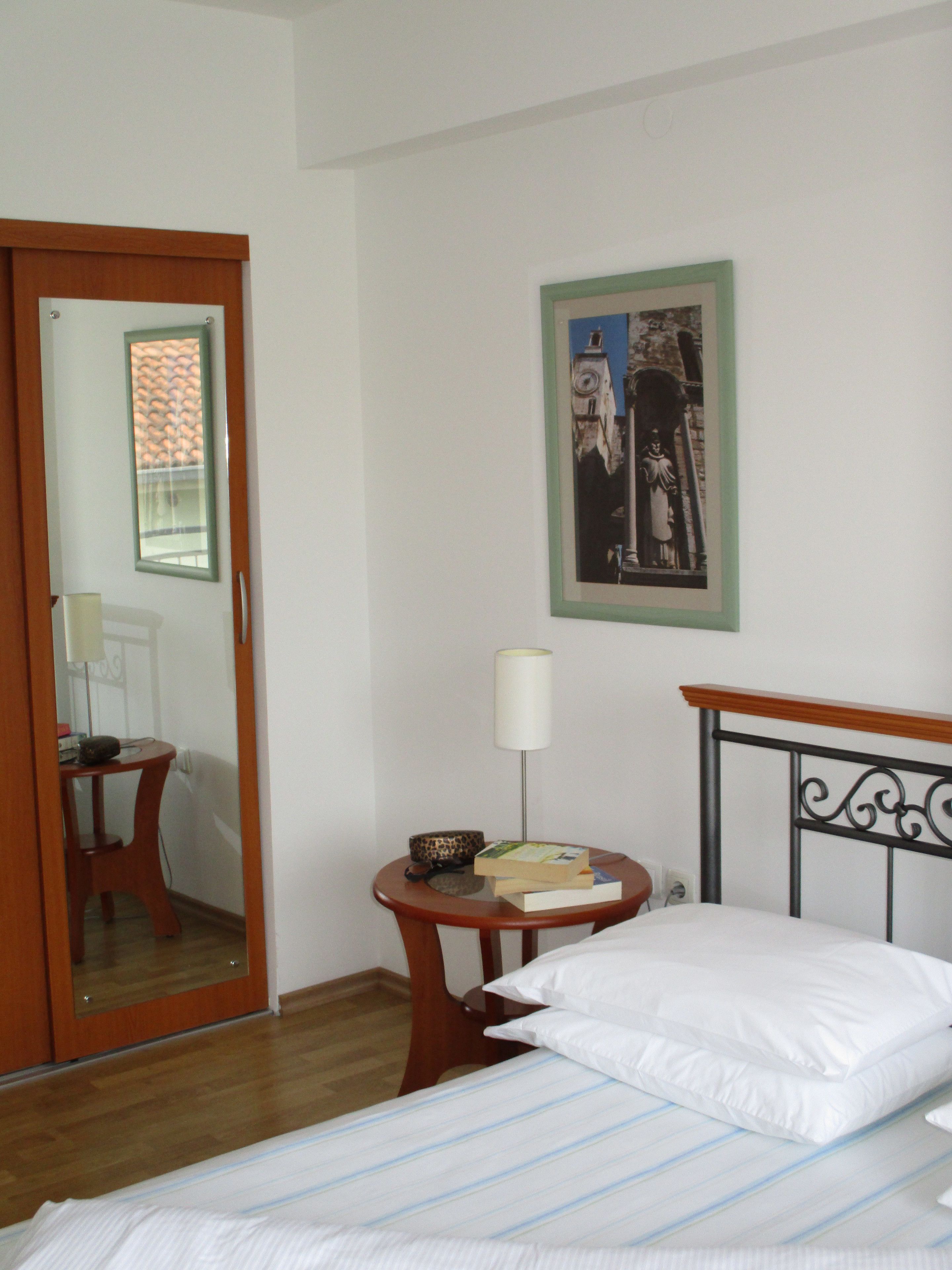 A hotel room with a bed, a round wooden table with a lamp, a framed picture on the wall, and a wooden door.