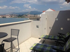 A balcony with a view of a city and mountains, featuring a table, two chairs, and a small table lamp.