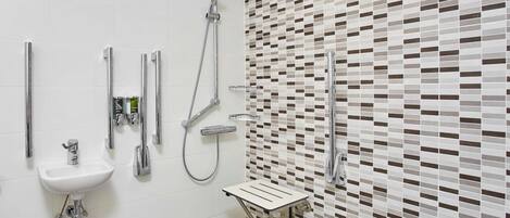 Un baño moderno con un lavamanos blanco, un cabezal de ducha manual, un toallero de pared y una zona de ducha con azulejos.