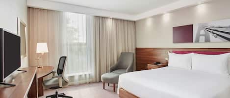 Ein Hotelzimmer mit Bett, Schreibtisch, Stuhl und einem großen Fenster mit Vorhängen.