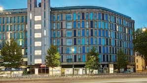 Ein modernes Hotel mit geschwungener Fassade, zahlreichen Fenstern und einem gut sichtbaren 'Hampton'-Schild.