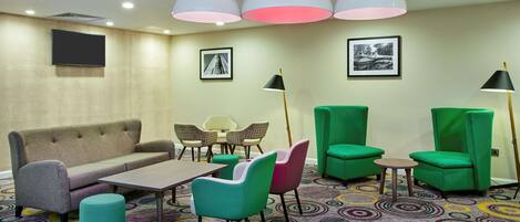 A hotel room with a sofa, two chairs, a small table, a patterned carpet, and two pendant lights.