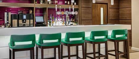 Eine Bar mit einer langen Theke, mehreren Barhocker und einer Auswahl an Flaschen und Gläsern.