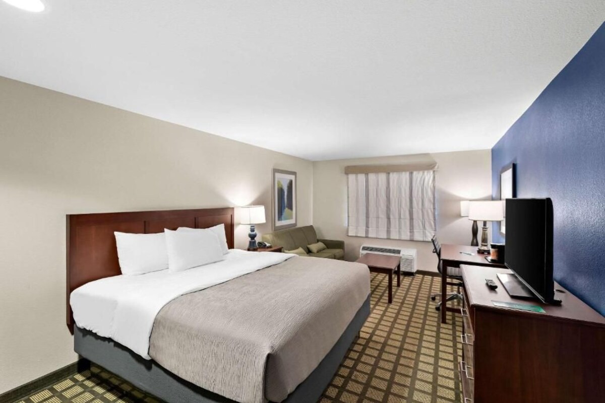 Quarto de hotel com cama, escrivaninha, televisão e janela com cortinas.