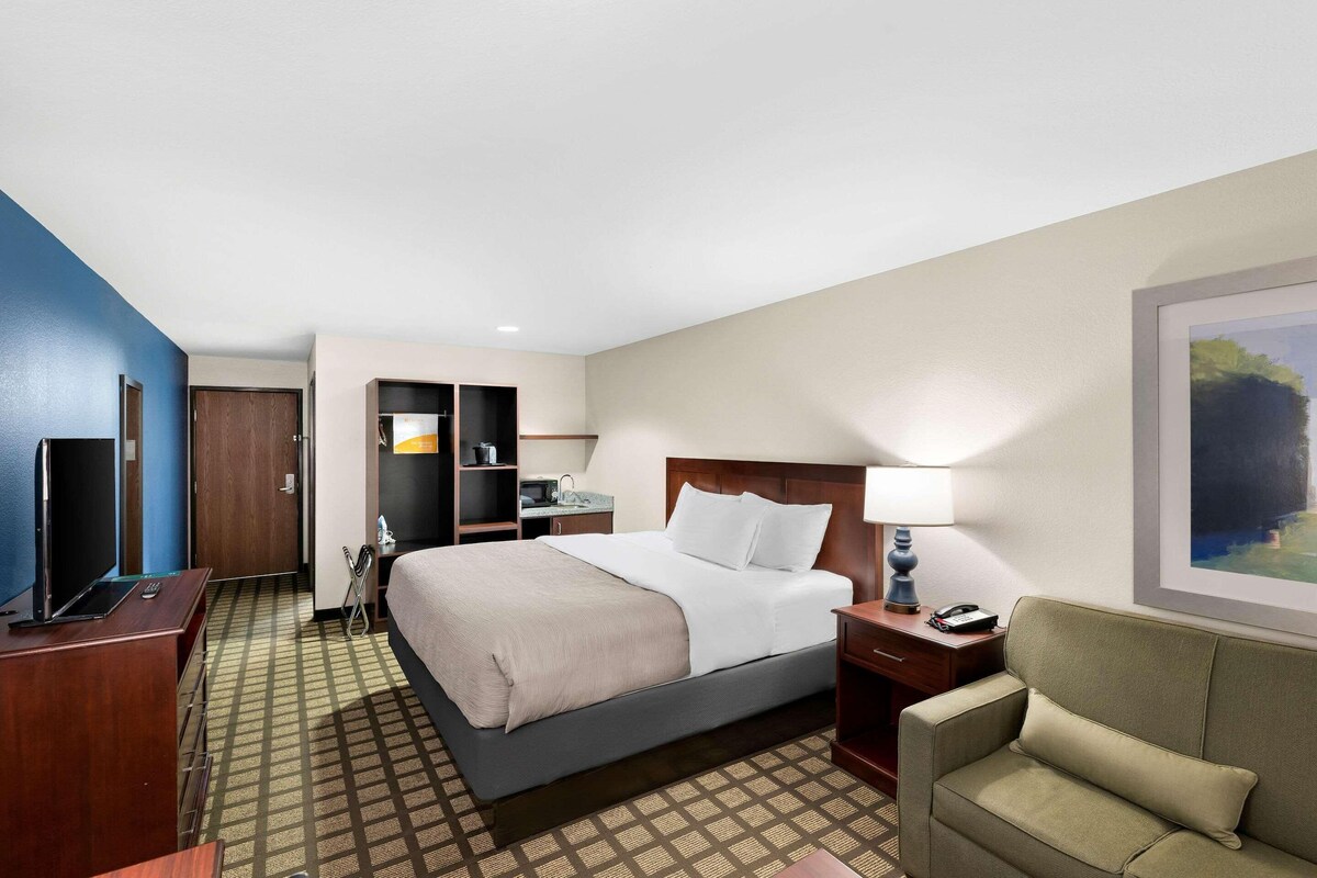 A hotel room with a bed, a desk, a chair, a TV, and a painting on the wall.