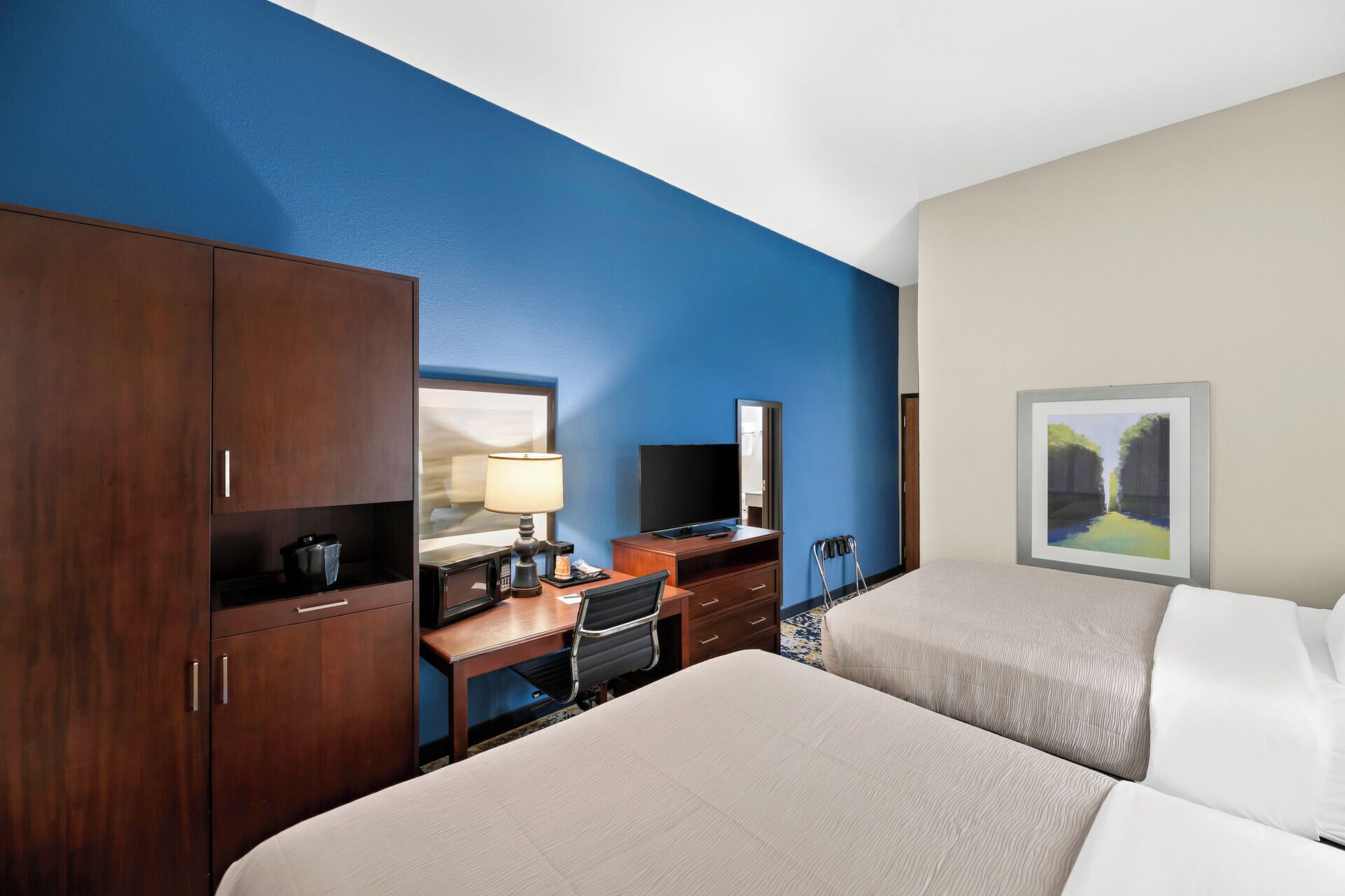 A hotel room with two beds, a desk with a computer, a TV, and a painting on the wall.