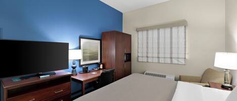 A hotel room with a large bed, a desk with a computer, a TV, and a window with blinds.