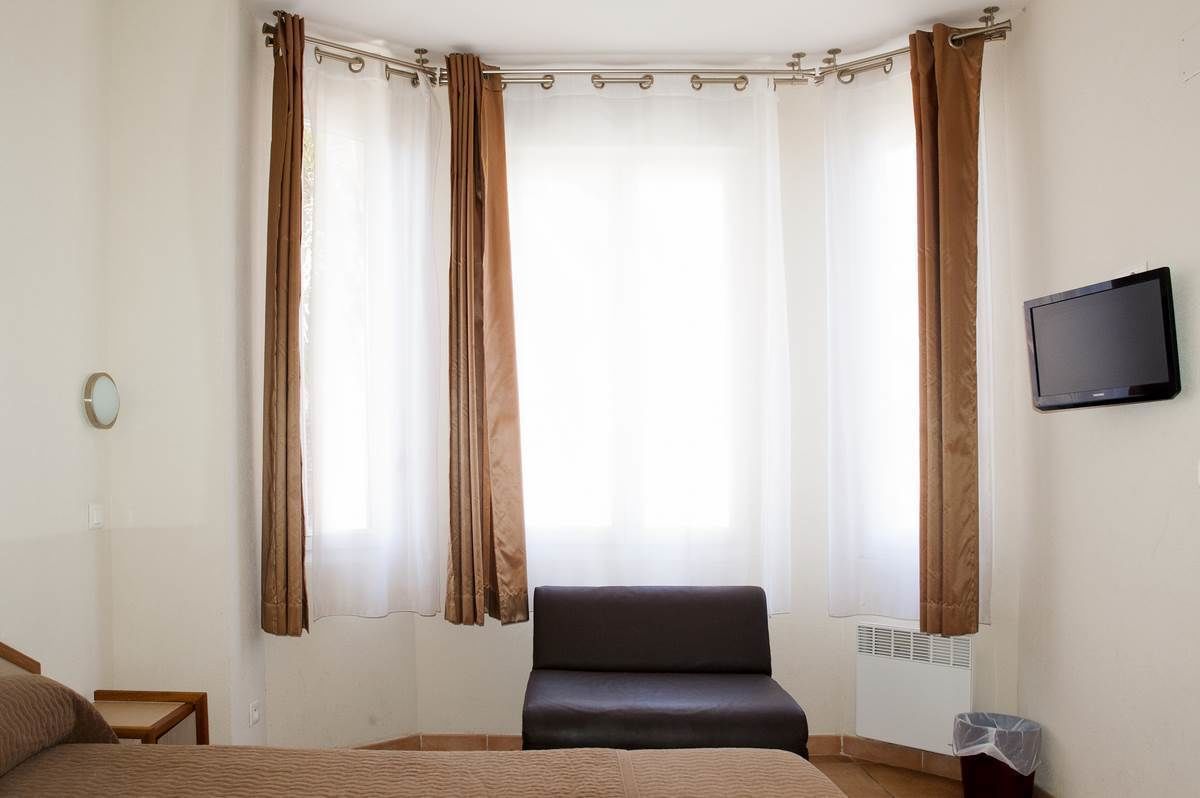 Un dormitorio con cama, una silla, televisor y ventana con cortinas.