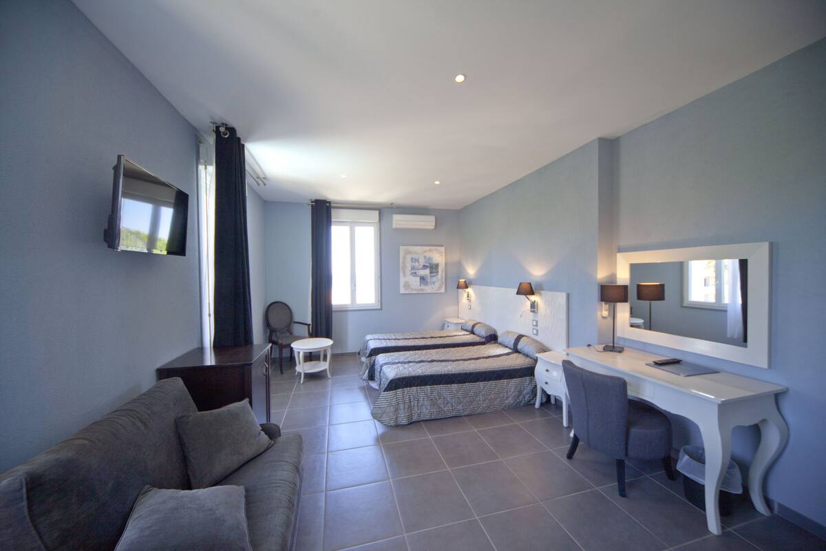 Quarto de hotel com sofá, duas camas, escrivaninha e televisão.