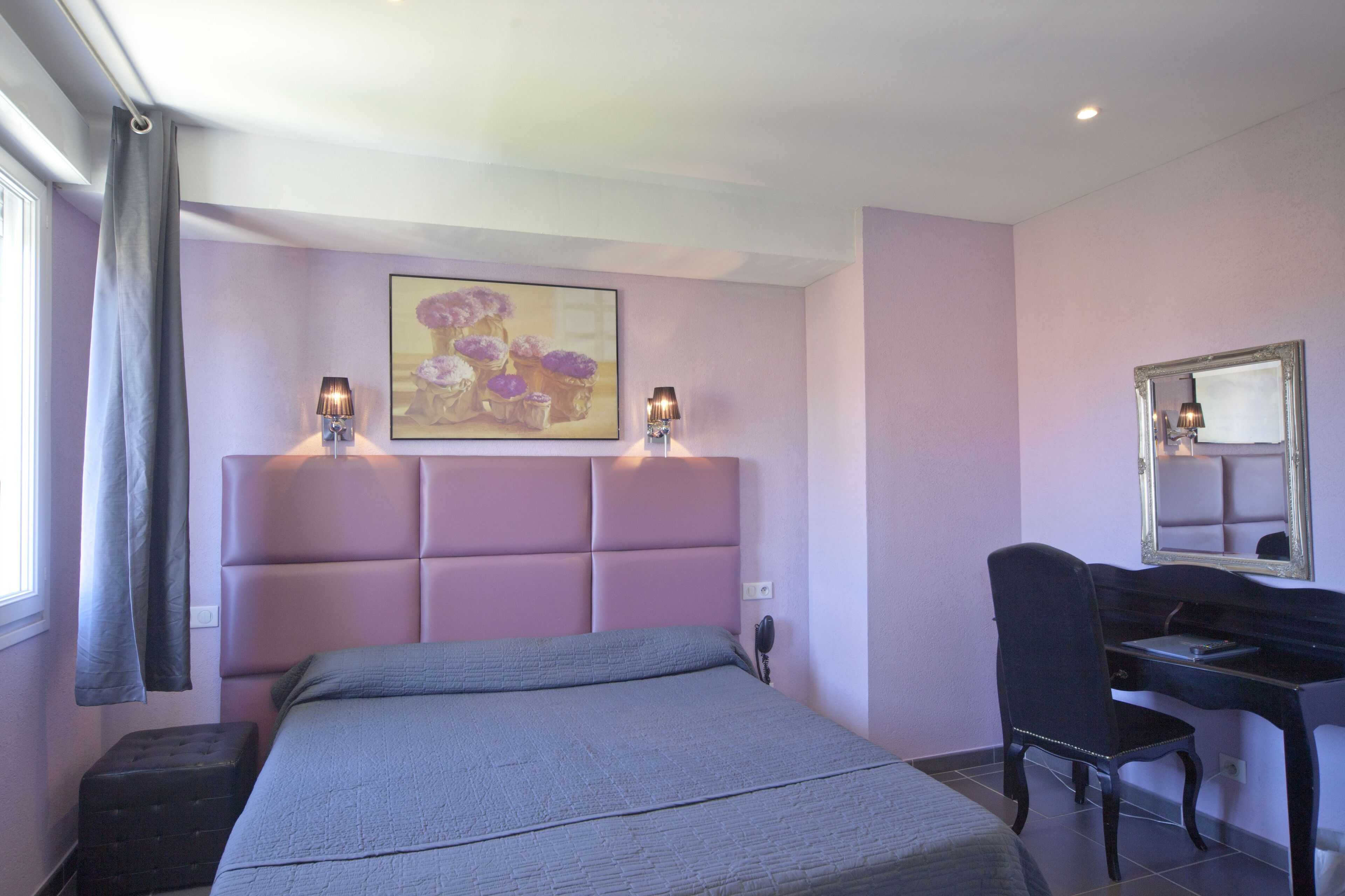 Un dormitorio con cama, escritorio, silla, un cuadro y un espejo.