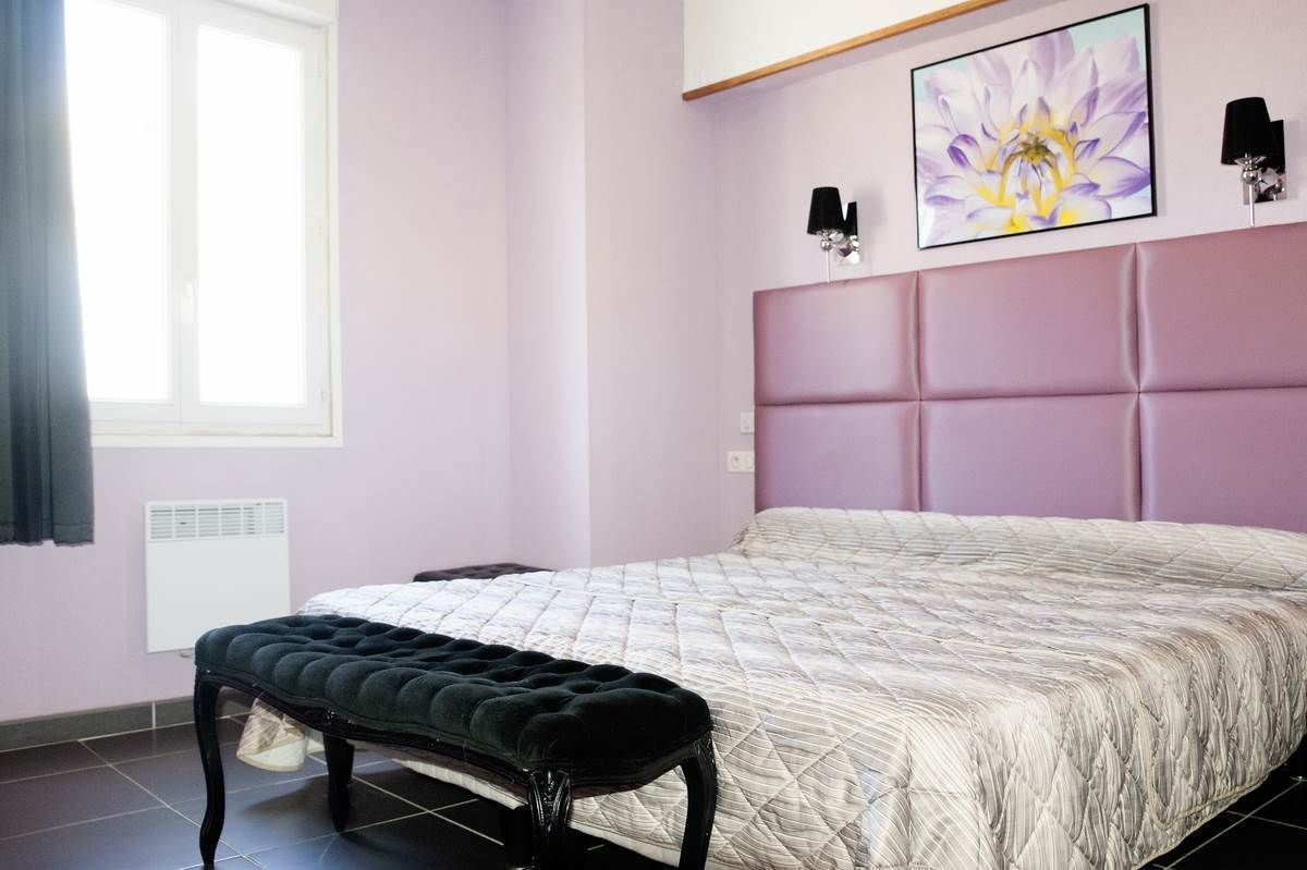 Un dormitorio con cama, banca, ventana y lámpara fijada a la pared.