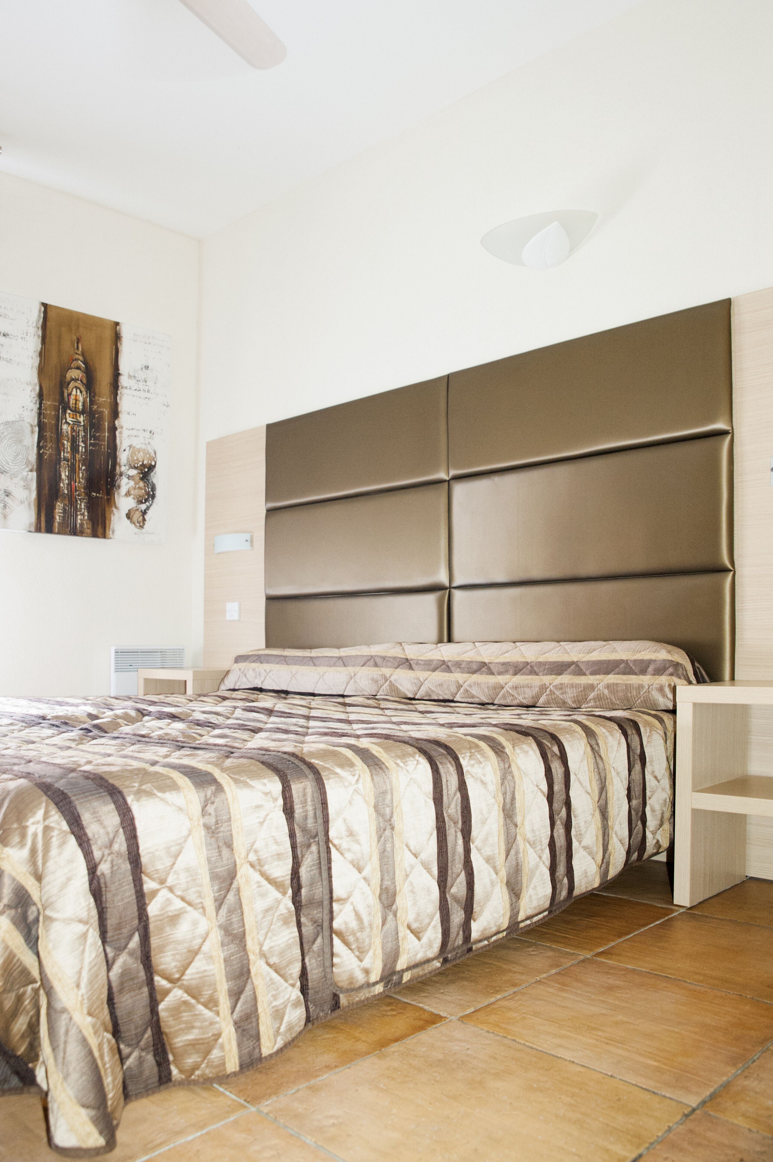 A bedroom with a bed, a headboard, a nightstand, and a wall-mounted artwork.