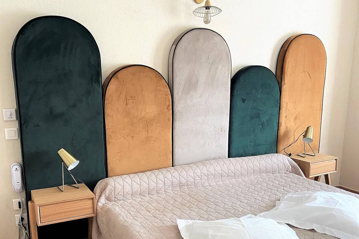 Quarto com cama, mesa de cabeceira, abajur e luminária na parede.