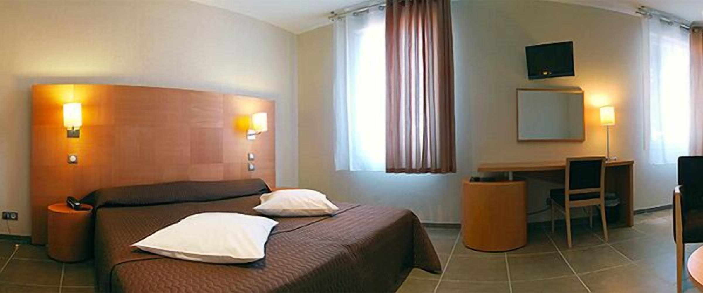A hotel room with a bed, bedside lamps, a desk, a chair, a television, and a window with curtains.