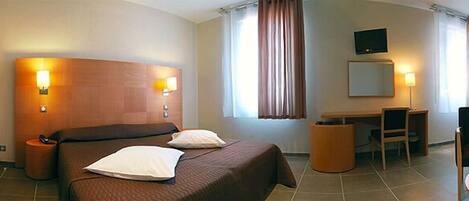 A hotel room with a bed, bedside lamps, a desk, a chair, a television, and a window with curtains.