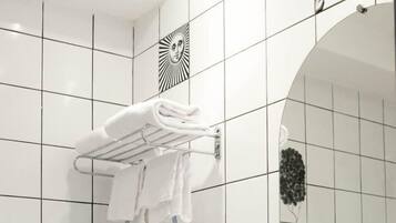 A bathroom with white tiles, a white sink, a glass shelf with towels, and a mirror with a decorative frame.