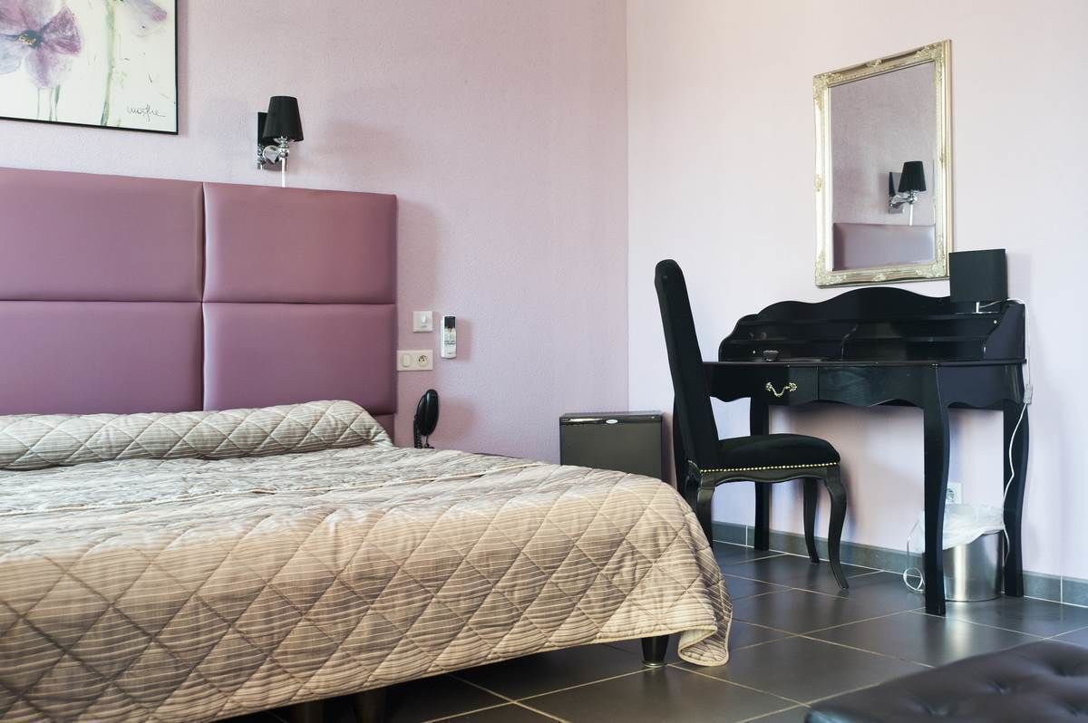 A hotel room with a bed, a desk, a chair, a mirror, and a lamp.